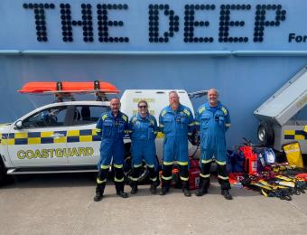 HM Coastguard team stood outside the front of The Deep building with their coastguard vehicle parked beside them.