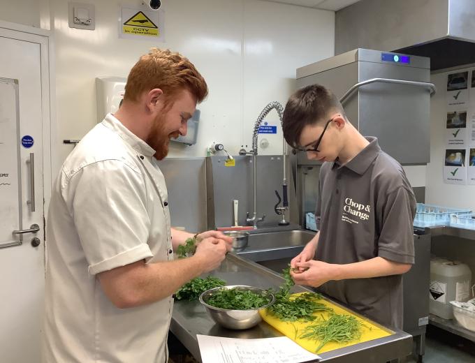 A Deep Crew member smiling and cutting vegetables with a student from Ganton School