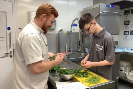 A Deep Crew member smiling and cutting vegetables with a student from Ganton School