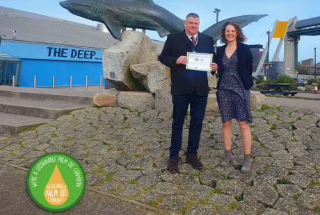 Rob from the University of Hull team stood with CEO of The Deep, Katy in front of The Deep's shark statue. They are holding a certificate and smiling.
