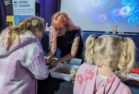 Two young girls making up hessian seed bags with the team at Yorkshire Wildlife Trust at The Deep's Seagrass Festival event.